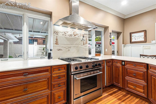 kitchen featuring backsplash, wall chimney range hood, stainless steel stove, ornamental molding, and light hardwood / wood-style floors