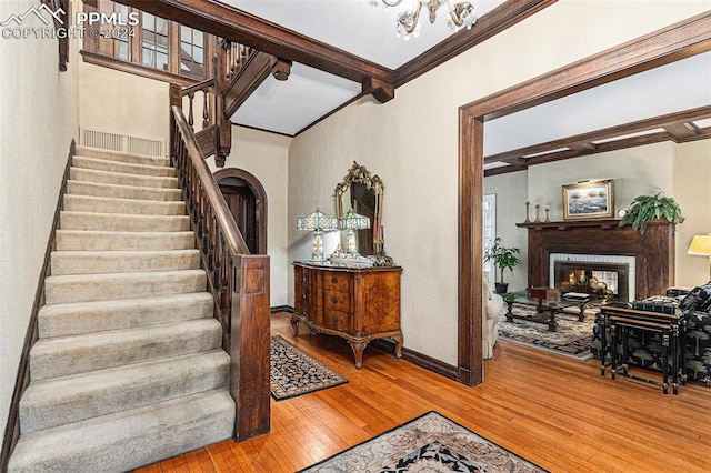 stairs featuring beamed ceiling, a multi sided fireplace, wood-type flooring, and crown molding