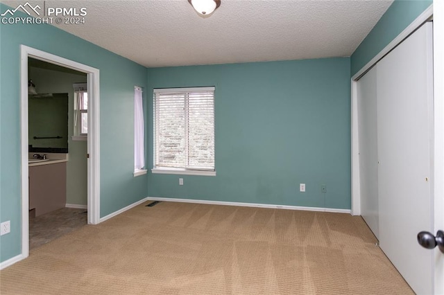 unfurnished bedroom with a textured ceiling, a closet, and light colored carpet