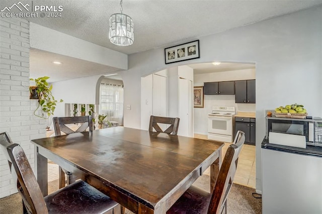 dining room featuring brick wall, a chandelier, light tile patterned flooring, and a textured ceiling