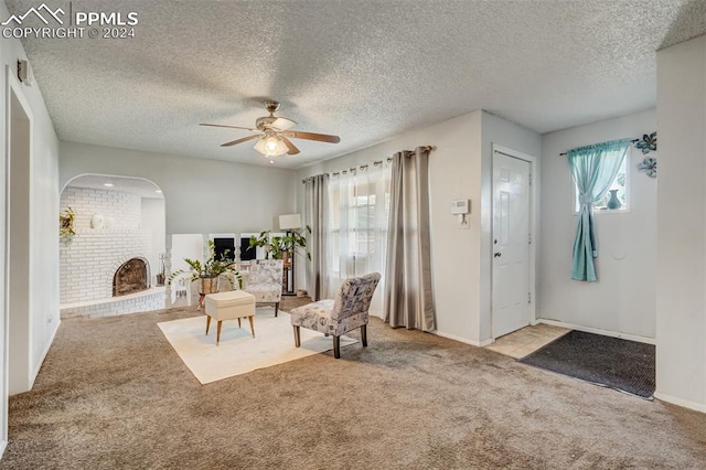 carpeted living room with a brick fireplace, a textured ceiling, and ceiling fan