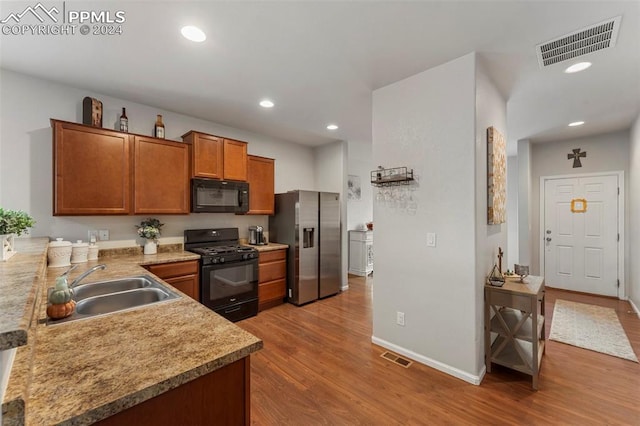 kitchen with sink, black appliances, light hardwood / wood-style flooring, and kitchen peninsula