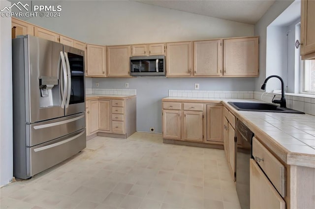 kitchen with light brown cabinetry, stainless steel appliances, tile counters, and lofted ceiling