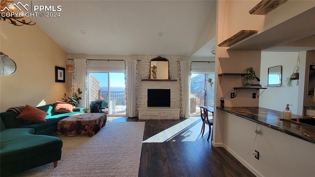 living room featuring a stone fireplace, dark hardwood / wood-style flooring, lofted ceiling, and a healthy amount of sunlight