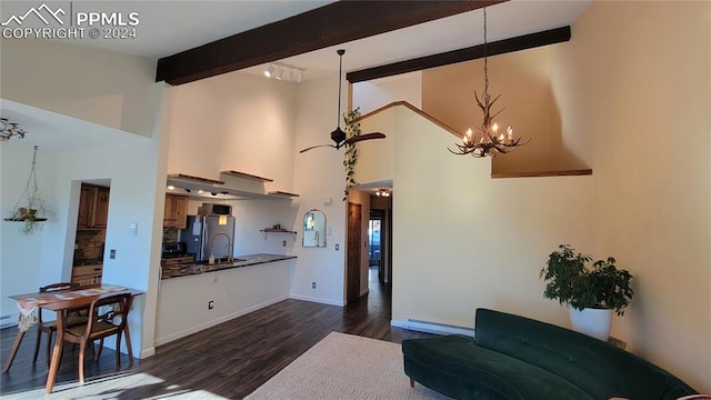 living room with dark wood-type flooring, a chandelier, baseboard heating, beamed ceiling, and a high ceiling