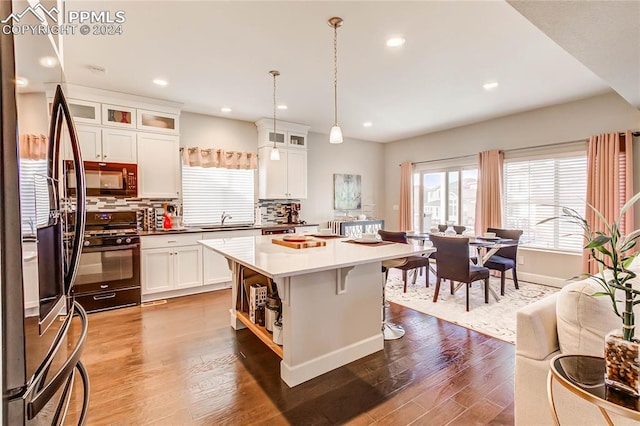 kitchen featuring hardwood / wood-style floors, tasteful backsplash, black appliances, decorative light fixtures, and a center island