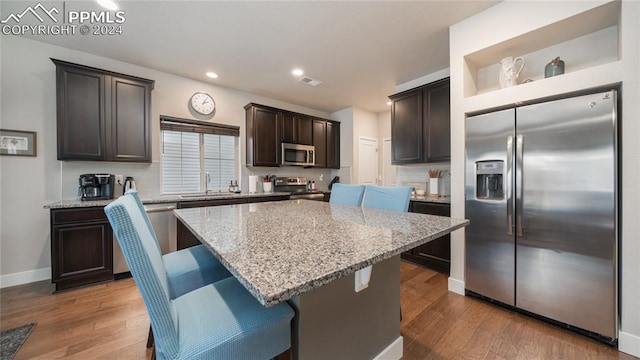 kitchen featuring light stone counters, appliances with stainless steel finishes, a breakfast bar, dark hardwood / wood-style floors, and a center island