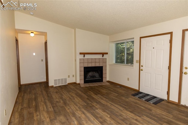 unfurnished living room featuring a textured ceiling, vaulted ceiling, a tiled fireplace, and dark hardwood / wood-style flooring