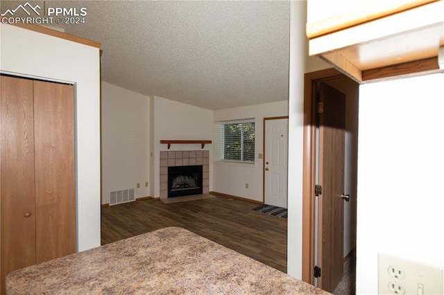 unfurnished living room with dark wood-type flooring, a tiled fireplace, and a textured ceiling