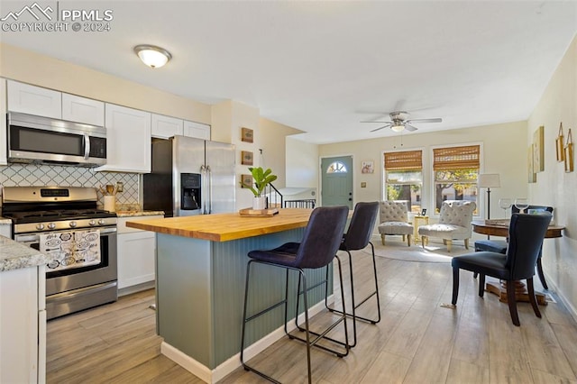 kitchen featuring light hardwood / wood-style flooring, stainless steel appliances, a breakfast bar, white cabinets, and butcher block countertops