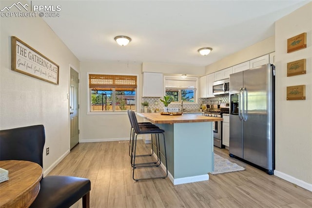 kitchen with wooden counters, white cabinets, a kitchen bar, light wood-type flooring, and appliances with stainless steel finishes