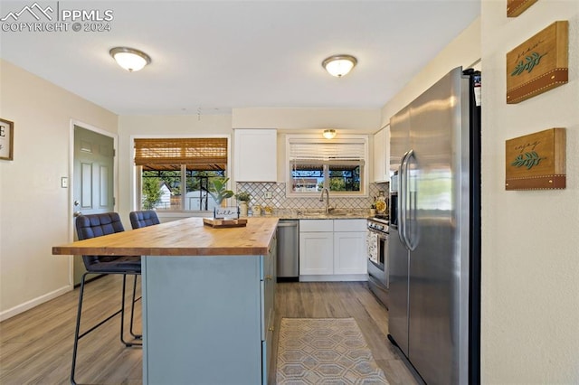 kitchen with white cabinets, a kitchen breakfast bar, butcher block counters, stainless steel appliances, and a center island