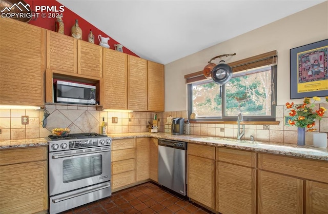 kitchen featuring vaulted ceiling, appliances with stainless steel finishes, sink, light stone countertops, and decorative backsplash