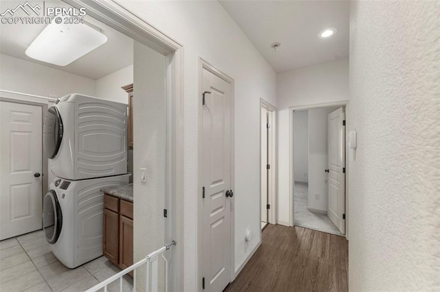 laundry area with cabinets, stacked washer / dryer, and light wood-type flooring