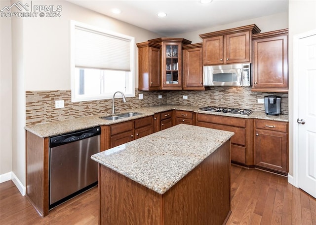 kitchen with a center island, sink, light stone countertops, appliances with stainless steel finishes, and wood-type flooring