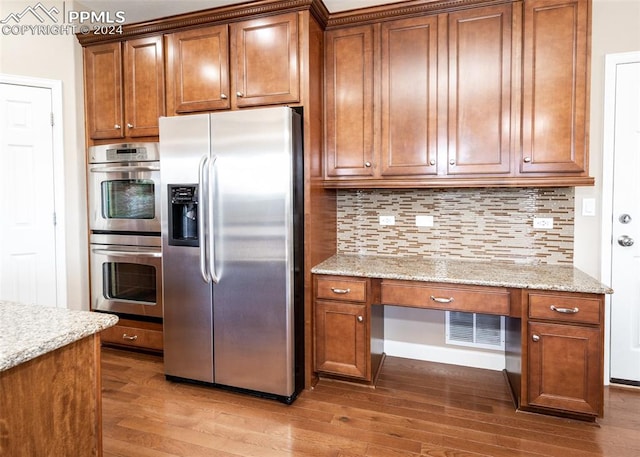 kitchen featuring decorative backsplash, light stone countertops, built in desk, wood-type flooring, and stainless steel appliances