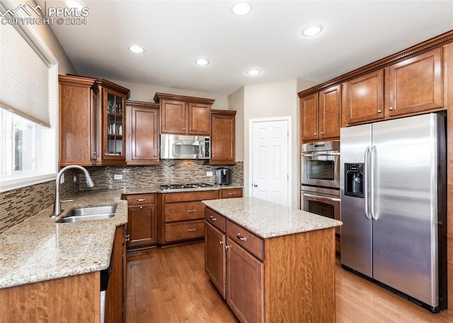 kitchen with a center island, sink, light stone countertops, light wood-type flooring, and stainless steel appliances