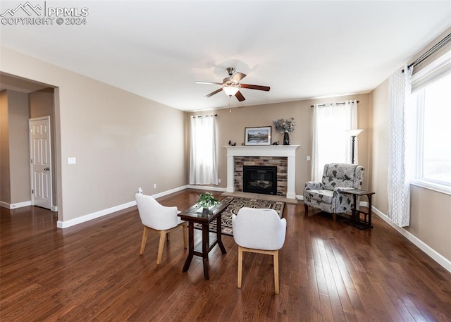 living room featuring a stone fireplace, ceiling fan, a healthy amount of sunlight, and dark hardwood / wood-style floors