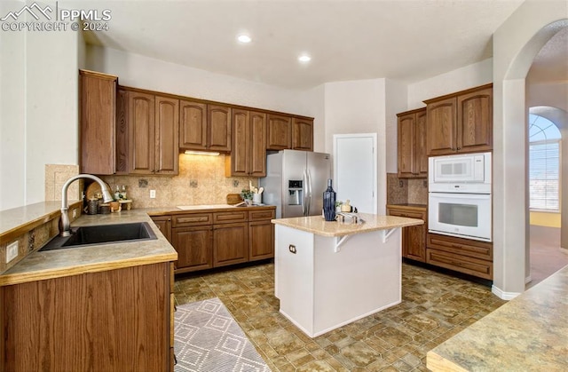 kitchen featuring sink, a kitchen breakfast bar, backsplash, white appliances, and a kitchen island