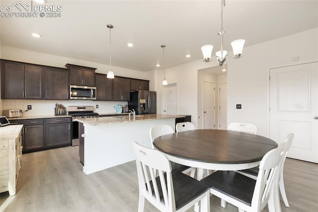 kitchen with a center island with sink, light wood-type flooring, pendant lighting, dark brown cabinetry, and stainless steel appliances