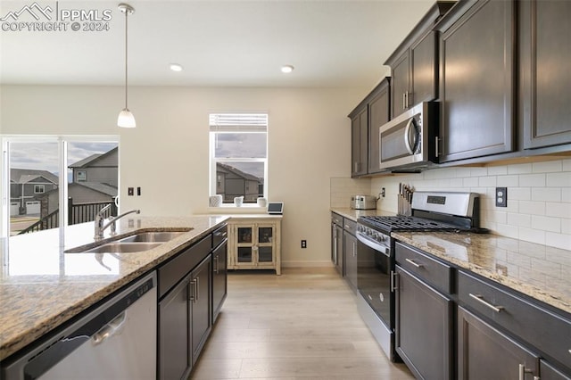 kitchen featuring light stone countertops, appliances with stainless steel finishes, sink, light hardwood / wood-style floors, and decorative light fixtures