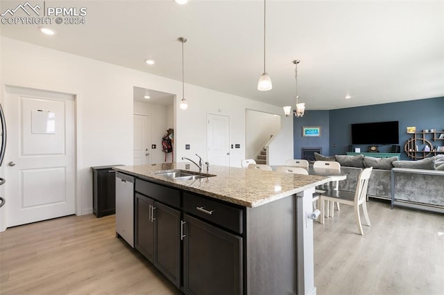 kitchen with decorative light fixtures, sink, light wood-type flooring, and a center island with sink