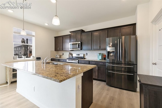 kitchen with stainless steel appliances, light stone countertops, dark brown cabinetry, pendant lighting, and light hardwood / wood-style floors