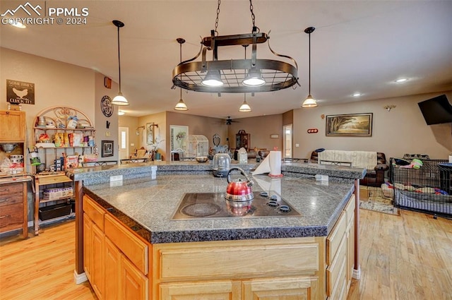 kitchen with electric stovetop, a large island with sink, and light wood-type flooring