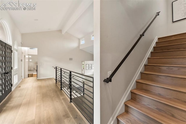 staircase with lofted ceiling with beams and wood-type flooring