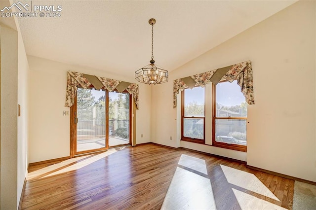 unfurnished dining area with lofted ceiling, a chandelier, and wood-type flooring