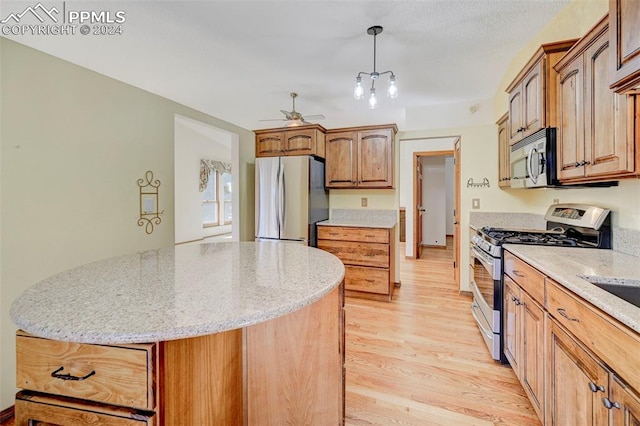 kitchen featuring appliances with stainless steel finishes, light stone countertops, light wood-type flooring, a center island, and decorative light fixtures