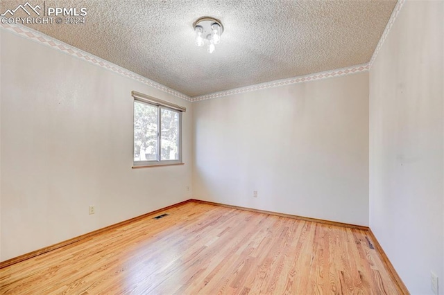 empty room with crown molding, a textured ceiling, and light wood-type flooring