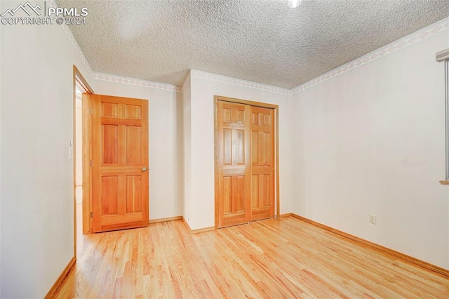 unfurnished bedroom with a closet, crown molding, a textured ceiling, and light wood-type flooring