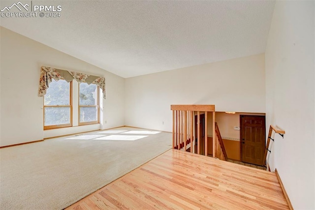 unfurnished room featuring hardwood / wood-style flooring, a textured ceiling, and lofted ceiling