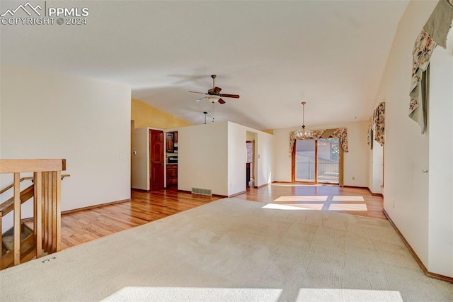 empty room featuring wood-type flooring, ceiling fan with notable chandelier, and vaulted ceiling