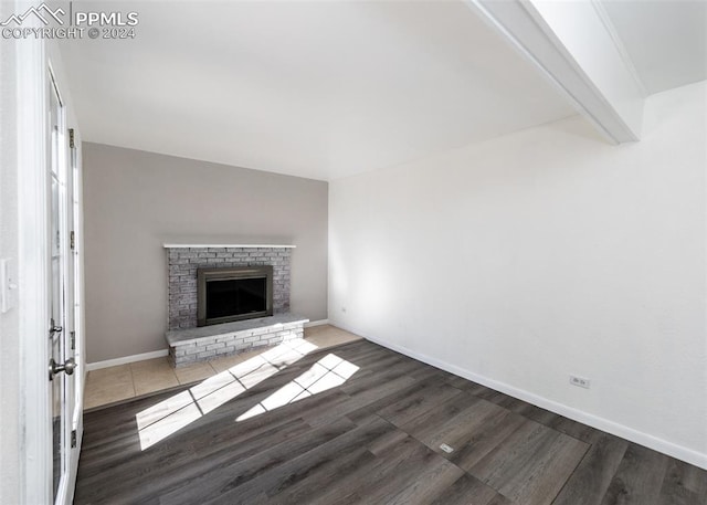 unfurnished living room featuring beam ceiling, dark hardwood / wood-style flooring, and a brick fireplace