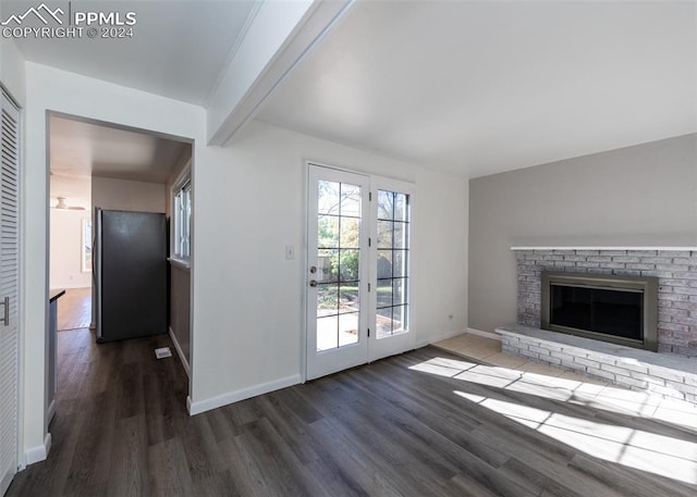 unfurnished living room with french doors, beam ceiling, a brick fireplace, and dark hardwood / wood-style floors