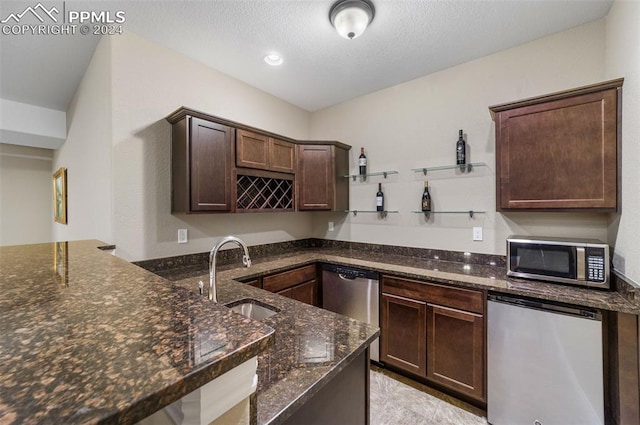 kitchen with dark brown cabinetry, appliances with stainless steel finishes, sink, and dark stone counters