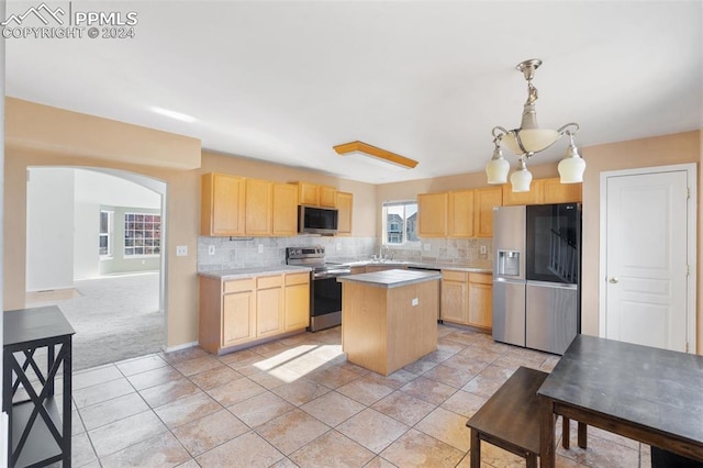 kitchen with appliances with stainless steel finishes, light brown cabinetry, hanging light fixtures, and a kitchen island