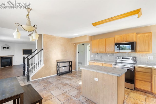 kitchen with a kitchen island, decorative backsplash, light brown cabinets, tile countertops, and appliances with stainless steel finishes