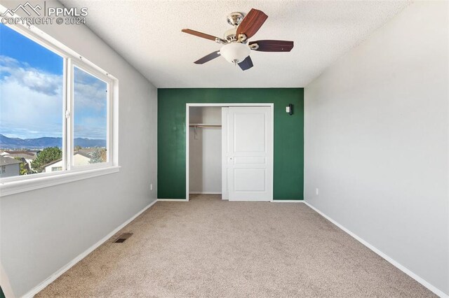 unfurnished bedroom featuring a closet, ceiling fan, multiple windows, and light colored carpet