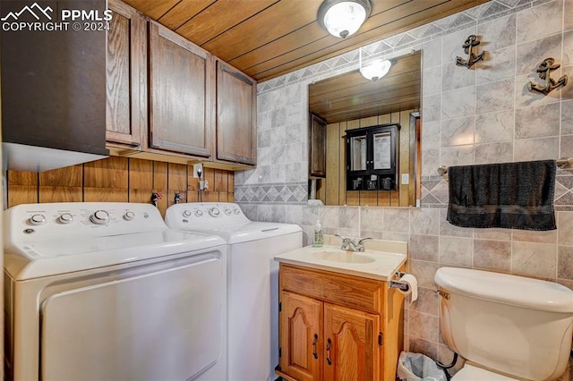 laundry room featuring washer and dryer, wooden ceiling, sink, and tile walls