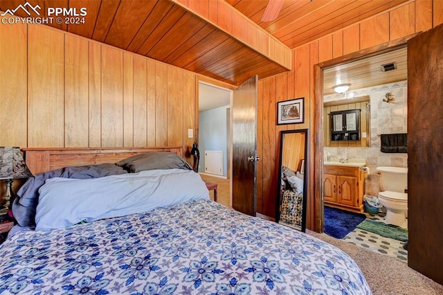 carpeted bedroom with wood ceiling, wooden walls, ensuite bath, sink, and ceiling fan