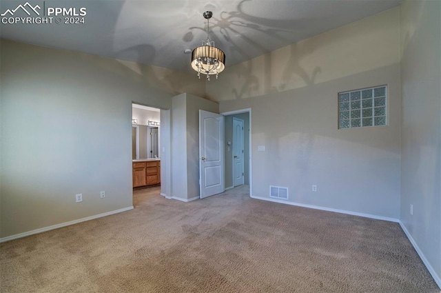 unfurnished bedroom with light carpet, a chandelier, and ensuite bath