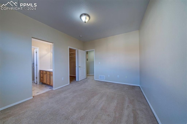 unfurnished bedroom with a spacious closet, light carpet, a closet, and ensuite bath