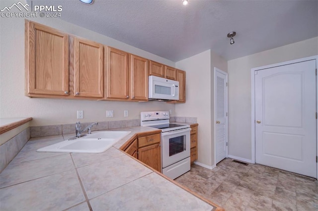 kitchen featuring a textured ceiling, light brown cabinetry, tile counters, sink, and white appliances