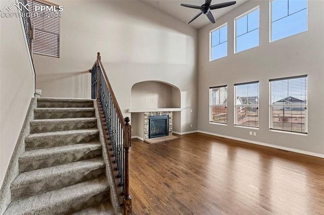 unfurnished living room featuring dark wood-type flooring, a stone fireplace, a towering ceiling, and plenty of natural light