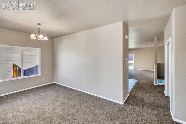 empty room with a textured ceiling, an inviting chandelier, and dark carpet