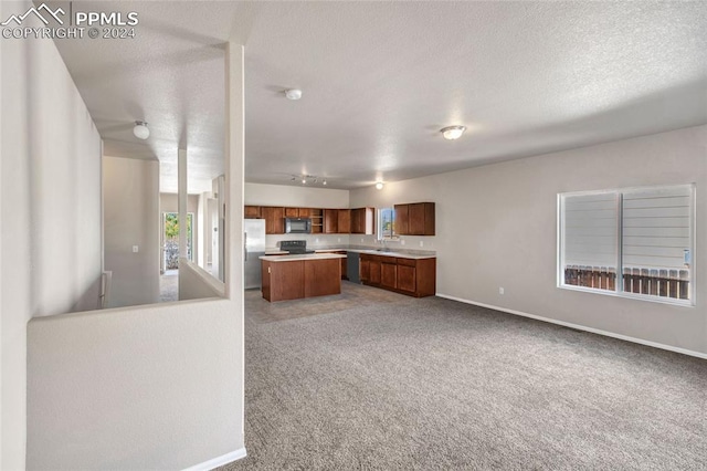 kitchen with light colored carpet, a center island, a textured ceiling, sink, and stainless steel refrigerator