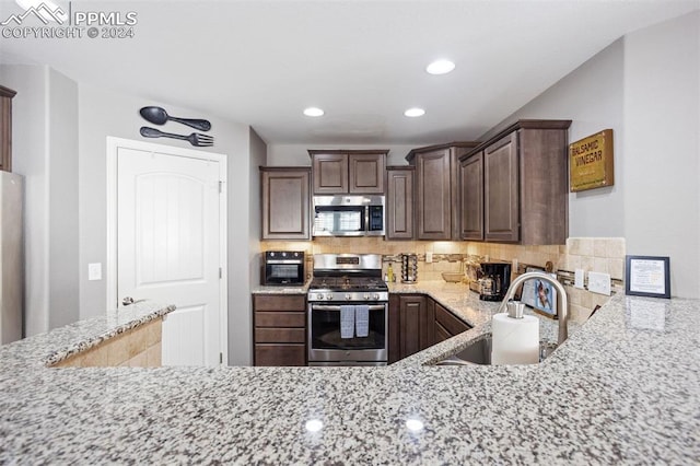 kitchen with sink, stainless steel appliances, light stone counters, decorative backsplash, and dark brown cabinets